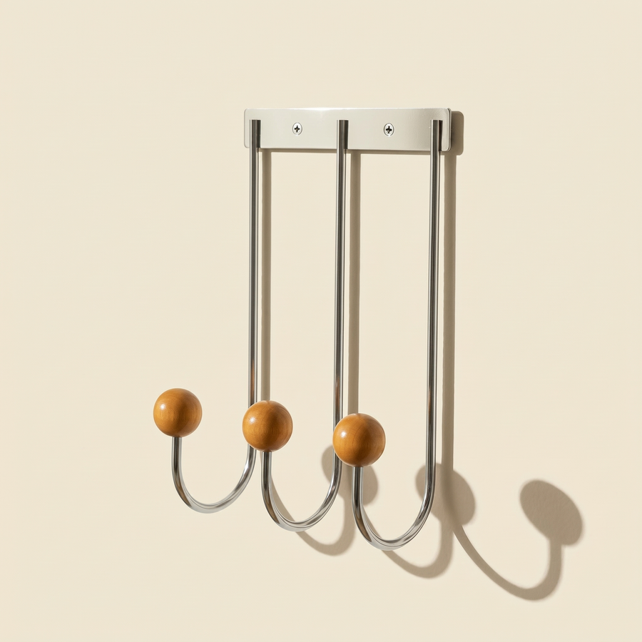 Sphere Hook Trio in stainless steel mounted on a wall, holding a coat and bag in an entryway