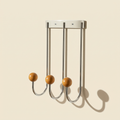 Sphere Hook Trio in stainless steel mounted on a wall, holding a coat and bag in an entryway
