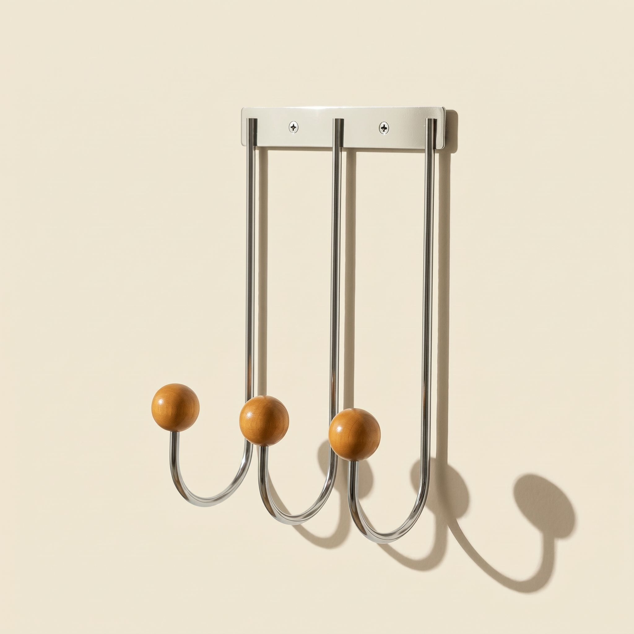 Sphere Hook Trio in stainless steel mounted on a wall, holding a coat and bag in an entryway